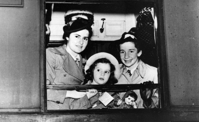 Bea on right with young girl in centre and older girl on left looking out train window towards camera