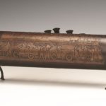 Brown Cylindrical Hanukah lamp, army scene carved into it, rear view