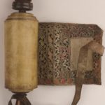 Parchment wrapped around wooden roller, see a bit of arabesque design showing from open bit of scroll on right, leather strap