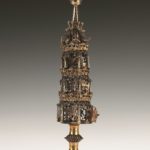 Silver three tiered spice box with floral designs and 6 figures from synagogue on top, steeple with ball and flag on top