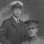 B & W Photo close up up one man standing on left in uniform and one sitting on right in different uniform