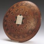 Wooden, circular plate with a white stone tablet on a black star of David in the centre.