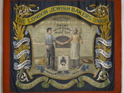 A red banner showing two bakers shaking hands in front of an oven. Above them are the words 'The London Jewish Bakers Union'.