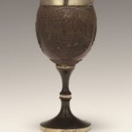 Brown cup made from coconut shell with silver rim. Carved image of men having a meal and using a Kiddush Cup.