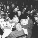 A black and white photograph showing people sat at two long tables