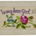 A white postcard with embroidered writing and flowers.