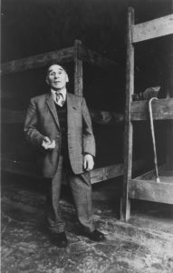 An elderly man - Leon Greenman - standing in front of bunk beds with walking stick hanging off the edge of one bunk