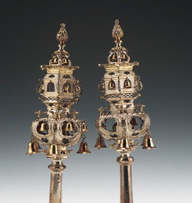 A pair of silver rimmonim against a faded grey to white background