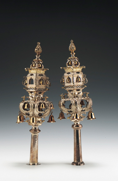 A pair of silver rimmonim against a faded grey to white background