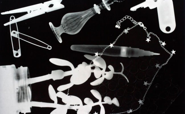 Black backfrop with white xray like images of objects including necklace, clothes peg, clothes pins and keys