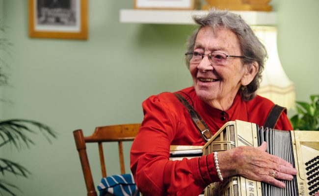 Bea Green, elderly lady, holding an accordian and smiling