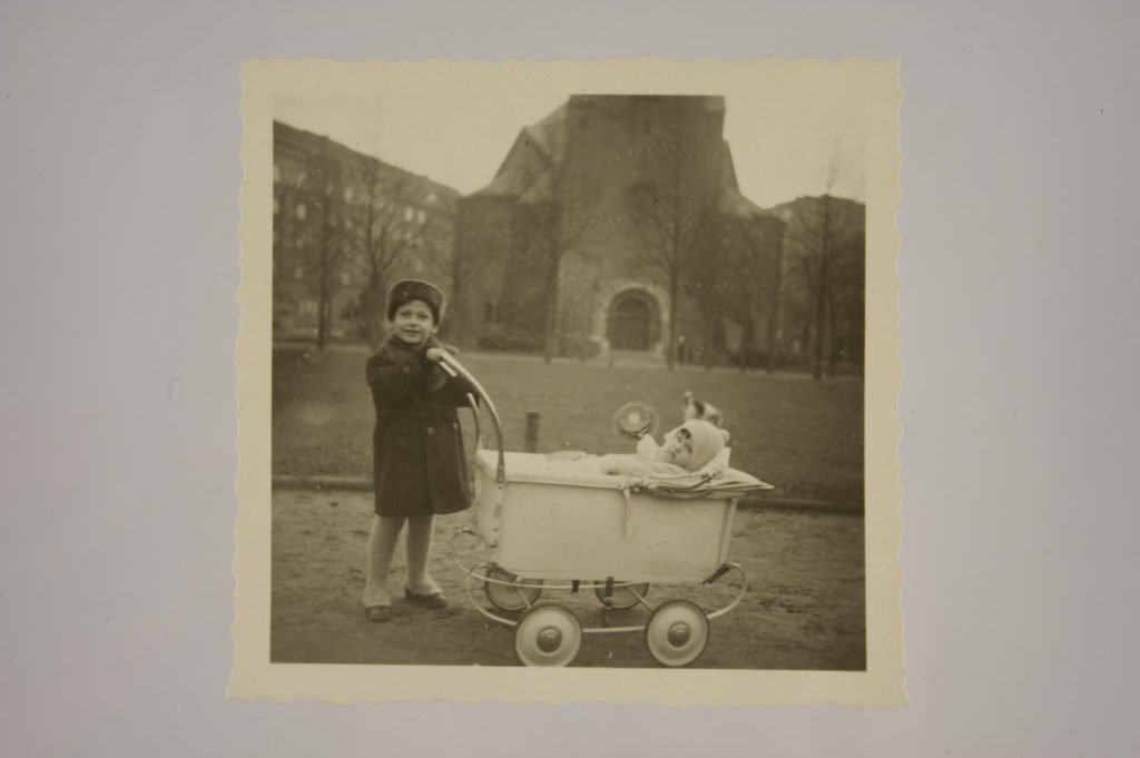 Young boy next to old style pram with a small infant inside