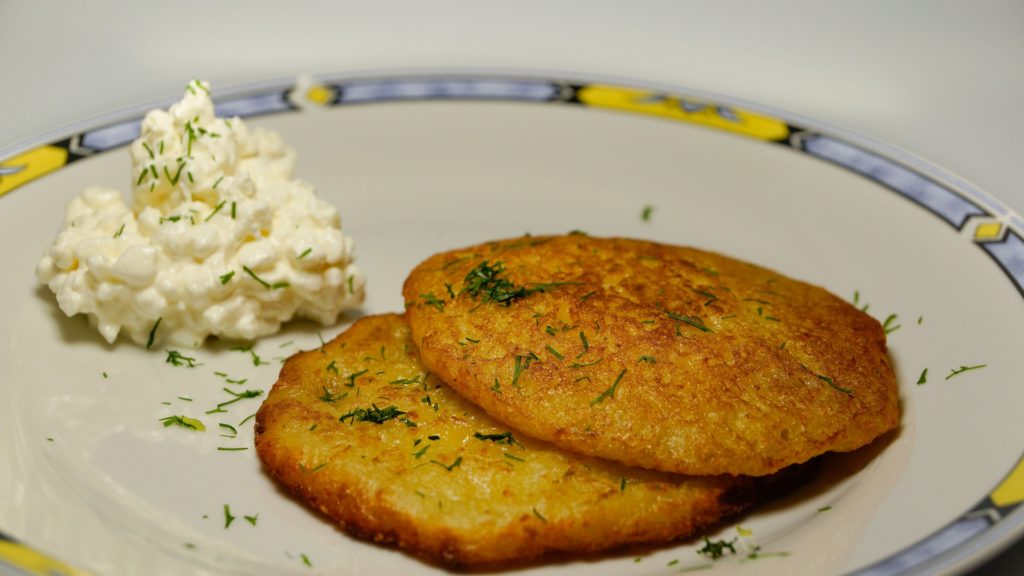 Two small potato latkes (pancakes) with herb garnish on a plate with a dollop of sour cream