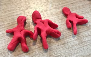 Three hand made red men made from Plasticine on a wooden surface