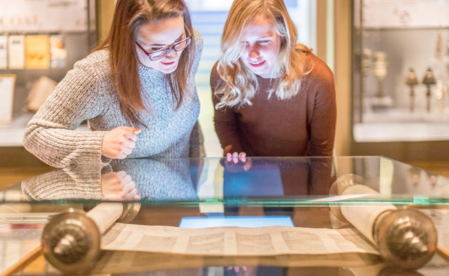 Two women looking at a paper scroll in a glass case