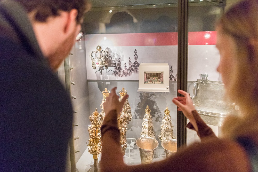 A man and a woman looking at silver objects in a glass case