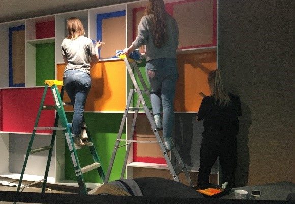 A group of people climbing up ladders in front of a colourful wall