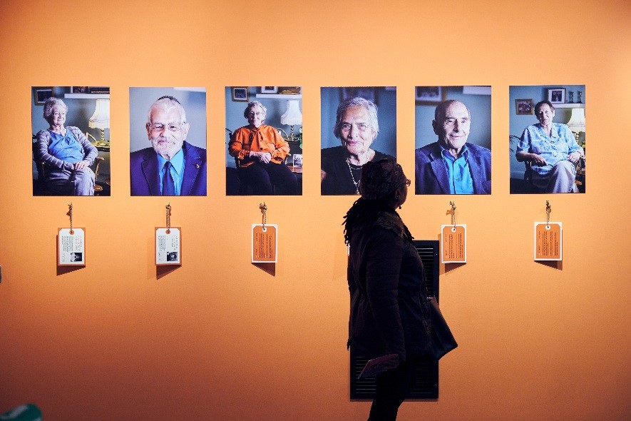 An orange wall with portraits on it and a person standing in front