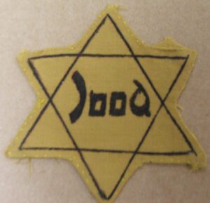 Yellow Badge in the shape of a star of David. Word Jood in the centre.